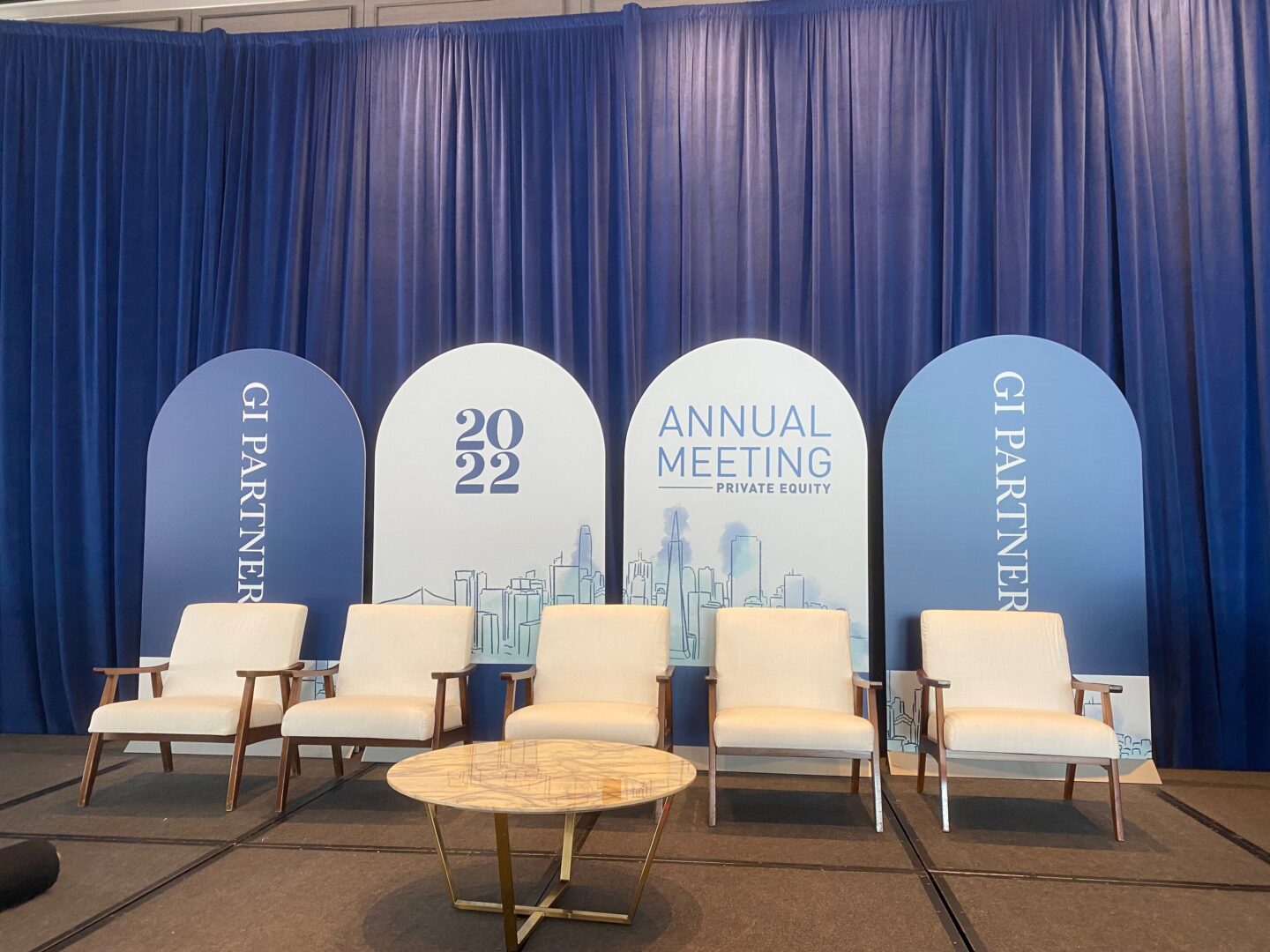 A group of chairs and tables in front of a wall with the names of the event.